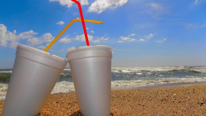 two polystyrene cups with straws on a beach.