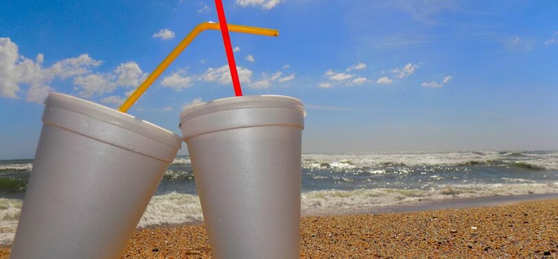 two polystyrene cups with straws on a beach.