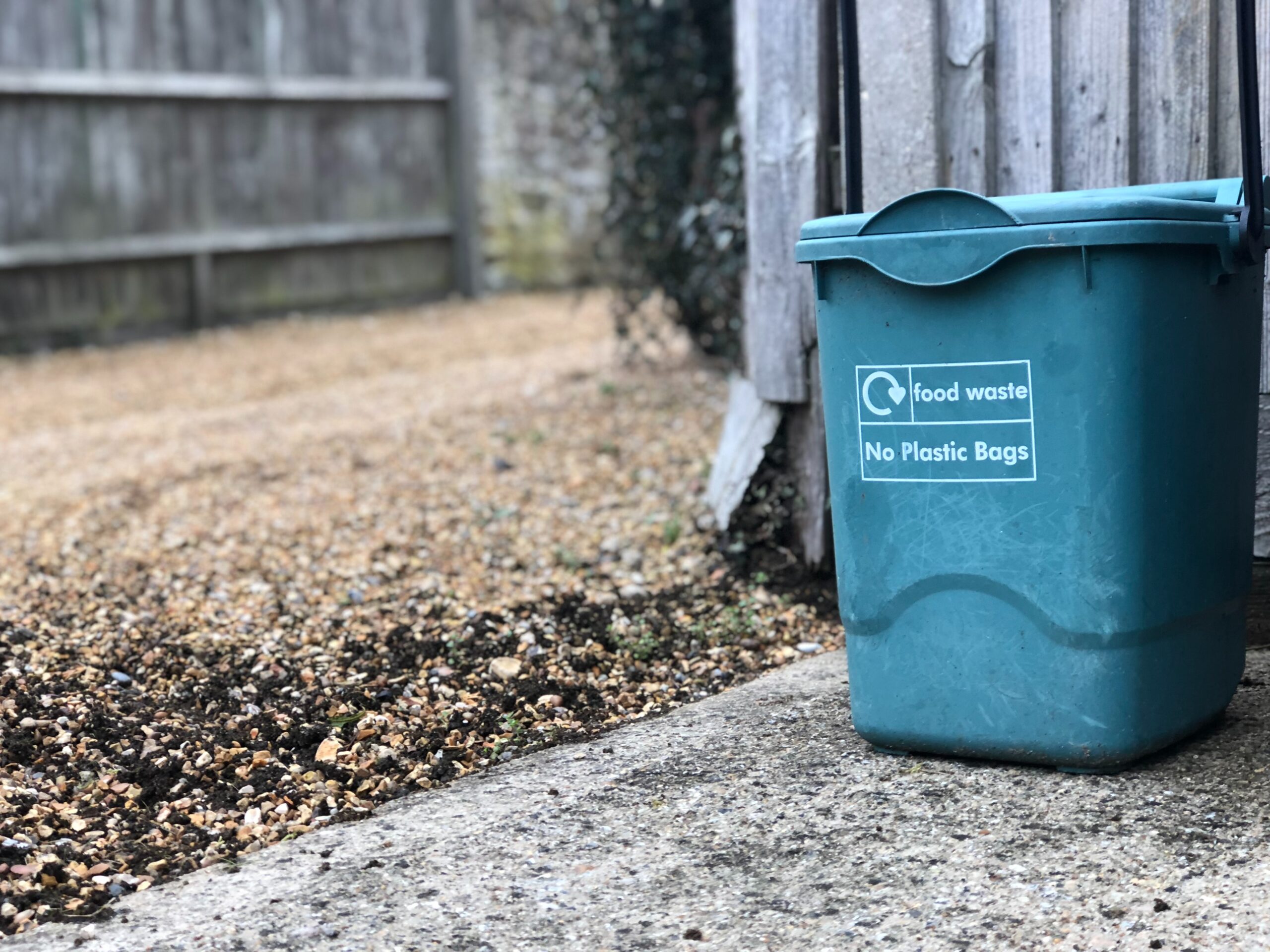 food waste bin in front of wooden fence.