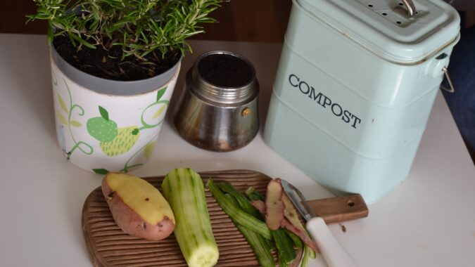 vegetables being peeled next to small compost bin on table.