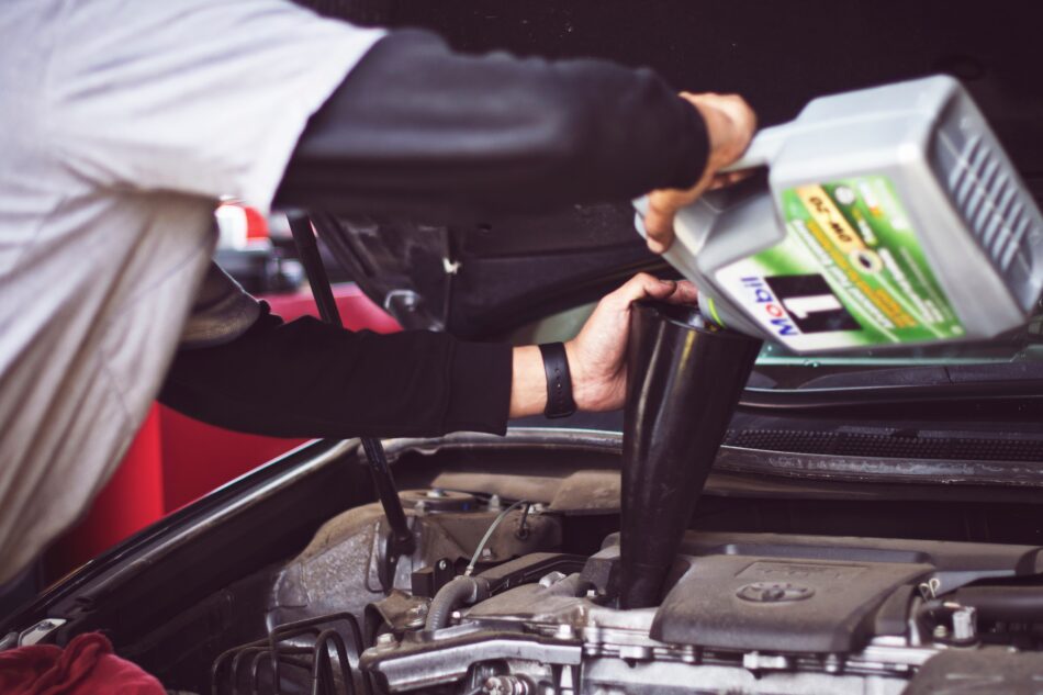 man pouring oil into car engine.