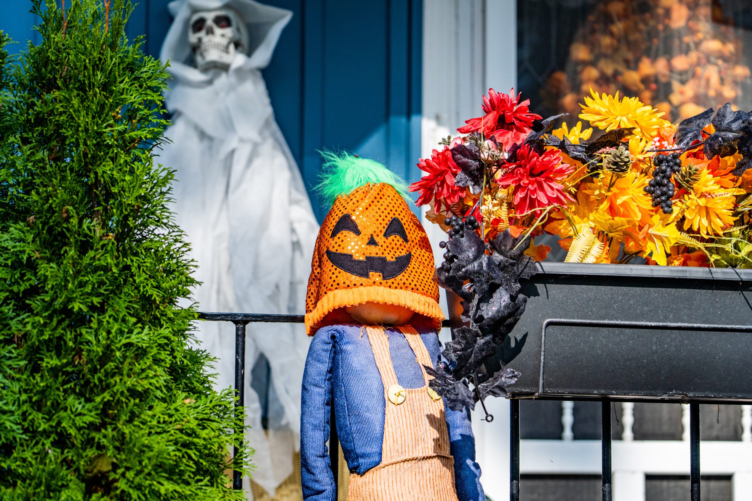scarecrow with pumpkin head stood outside house.