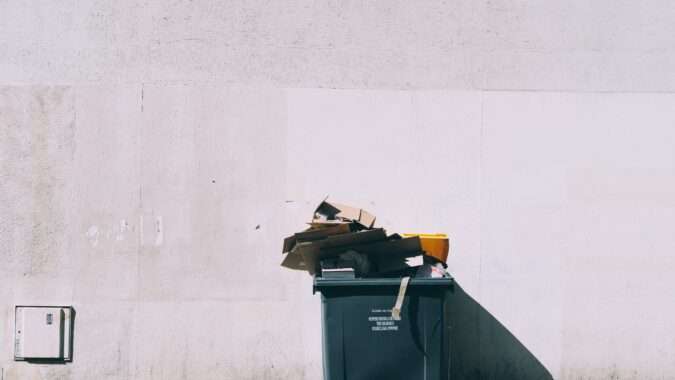 four wheel bin overflowing in front of white wall.