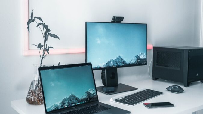 laptop and computer monitor with keyboard and tower on white desk.