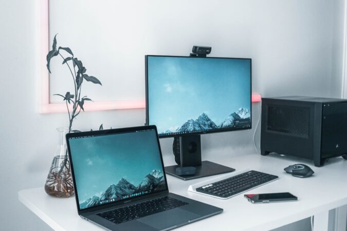 laptop and computer monitor with keyboard and tower on white desk.