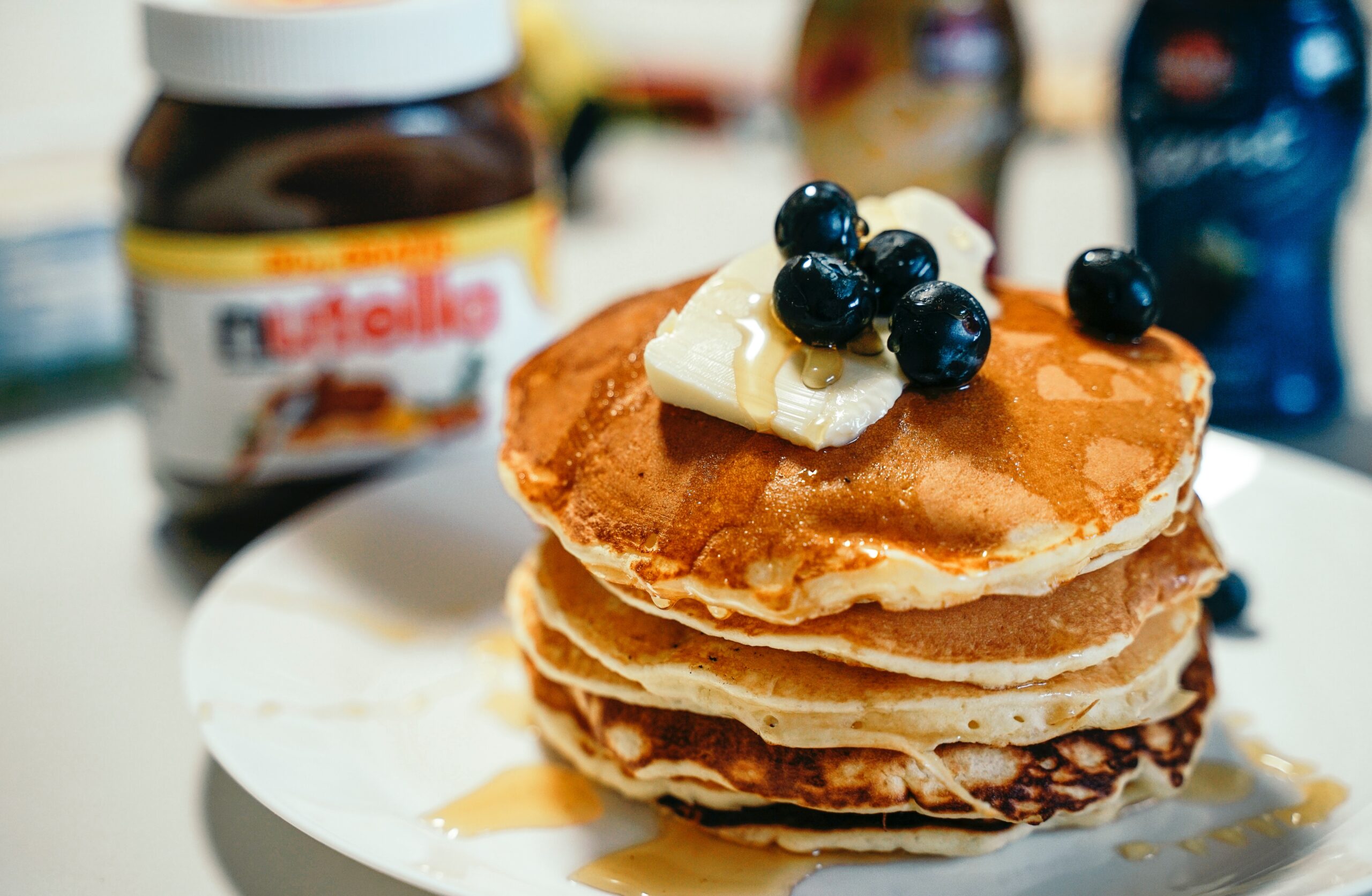 pancakes with blueberries on top and Nutella jar in background.