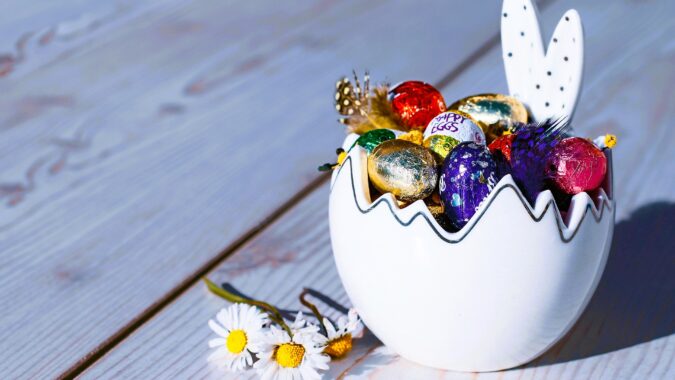 small foil Easter eggs in bunny bowl next to daisies.