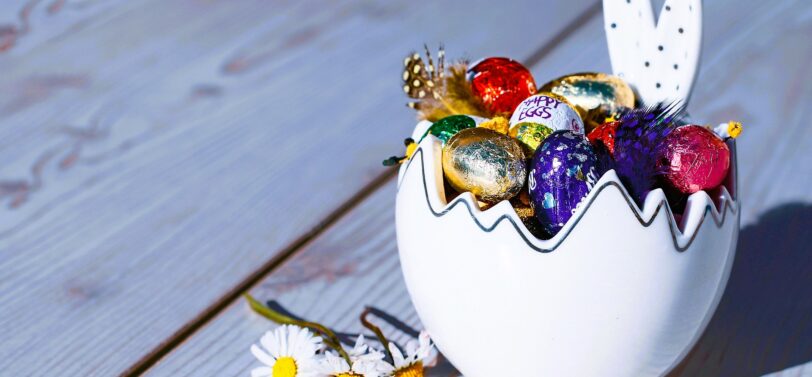 small foil Easter eggs in bunny bowl next to daisies.