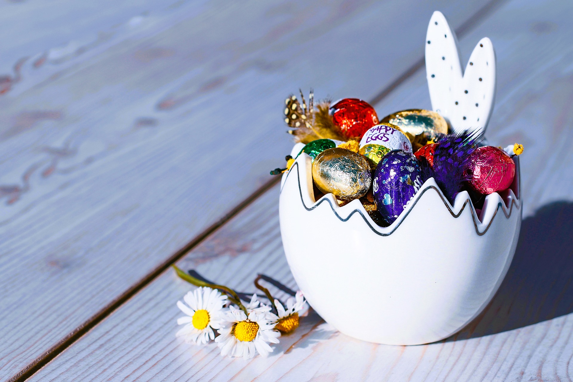 small foil Easter eggs in bunny bowl next to daisies.