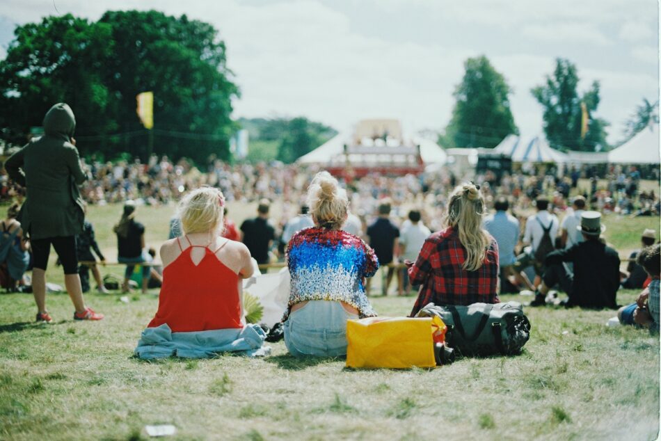 three women sat down in field in front of festival tent.