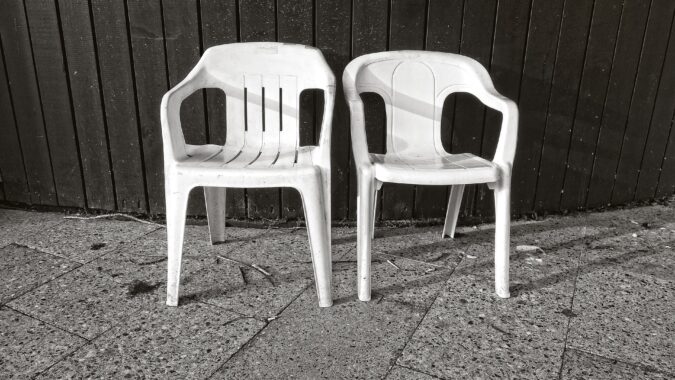 two white plastic garden chairs in front of fence.
