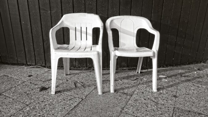two white plastic garden chairs in front of fence.