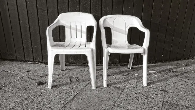 two white plastic garden chairs in front of fence.