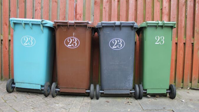 four wheelie bins lined up in front of fence.