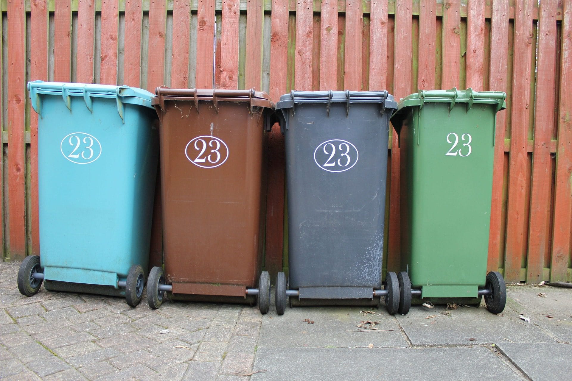 four wheelie bins lined up in front of fence.