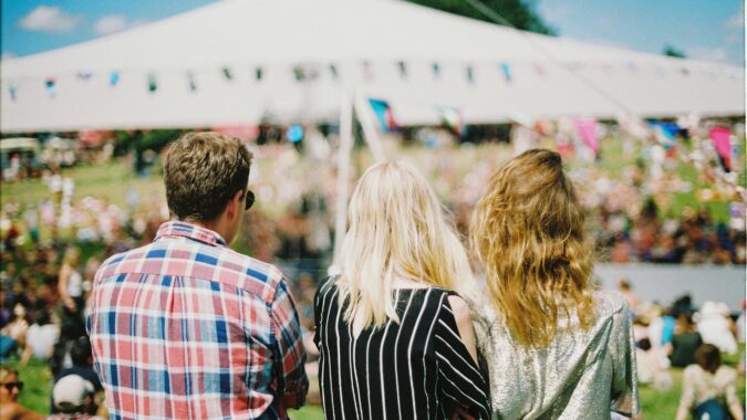 backs of three people sat in front of big tent at a festival.
