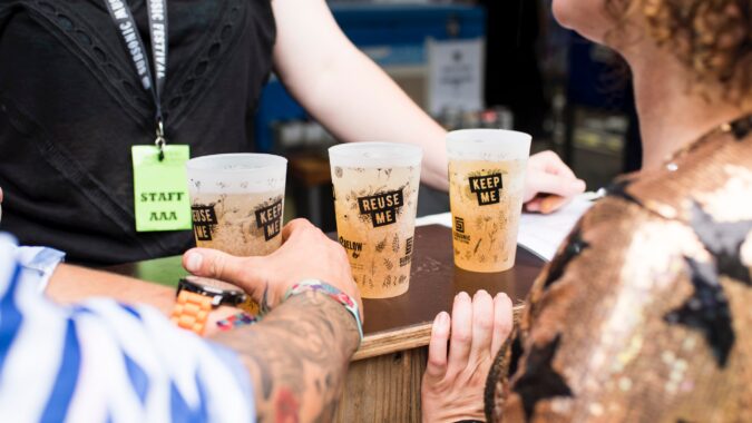 three plastic reusable cups full of beer at a festival.