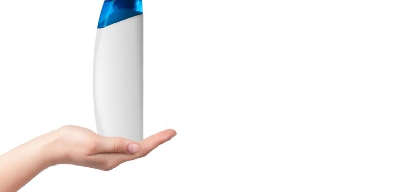 white HDPE plastic shampoo bottle held out on a hand.