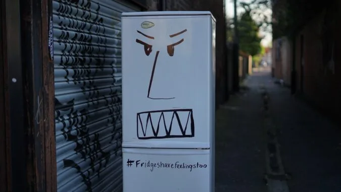 old fridge in backstreet with graffiti face.