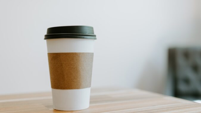 paper coffee cup with lid sat on a table.