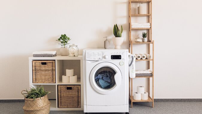 washing machine next to shelves and plant pot.