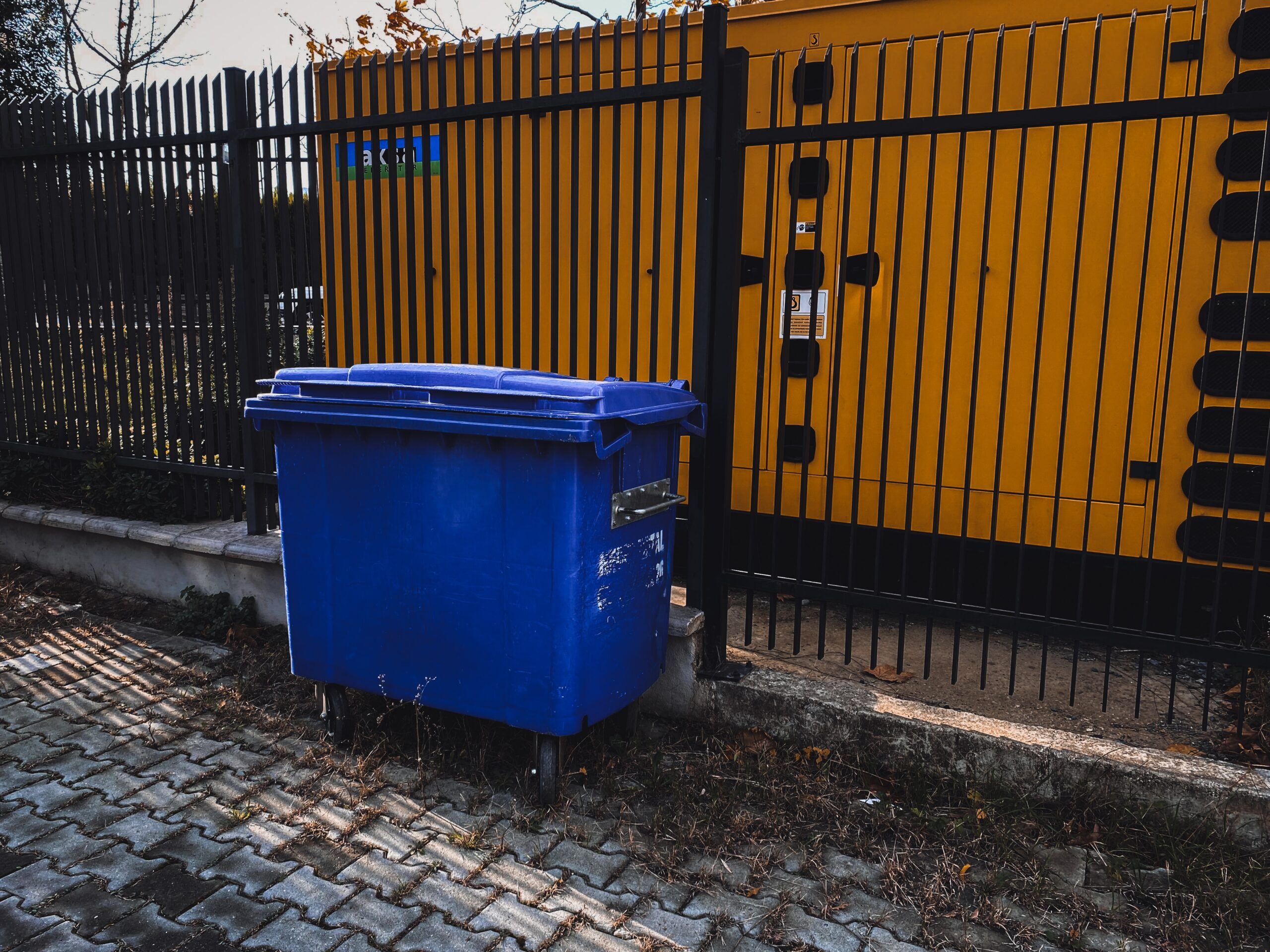 blue four wheel bin in front of a metal fence.