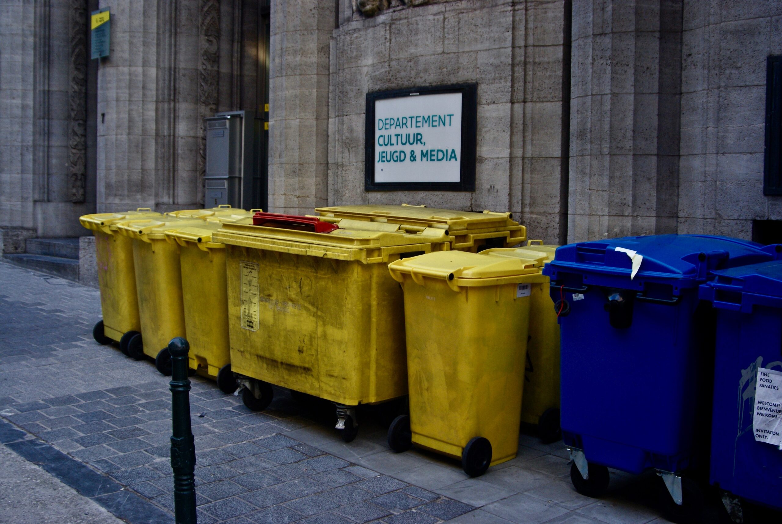 colleciton of two and four-wheel bins outside an important building.