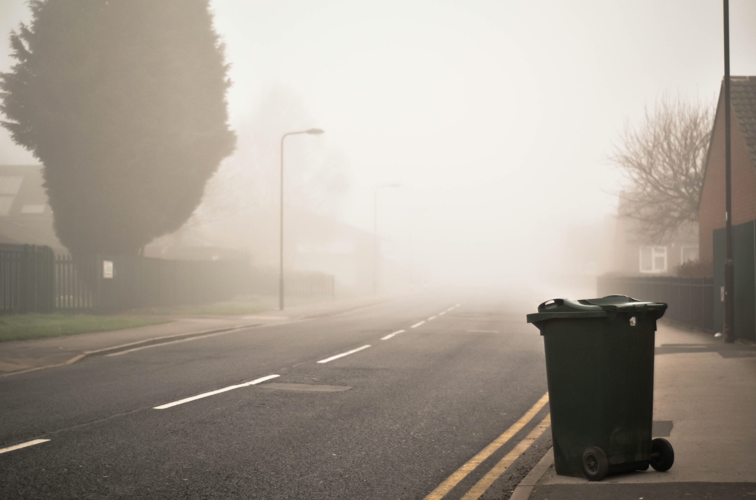 grey wheelie bin by the side of the road waiting for collection in fog.