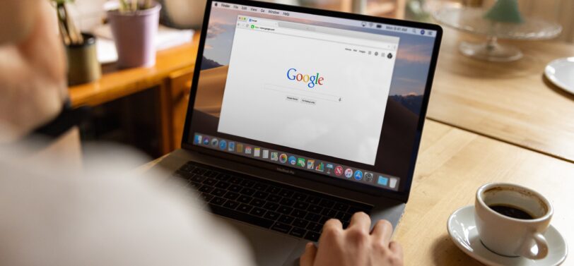 over shoulder of man using Google on laptop with a coffee.