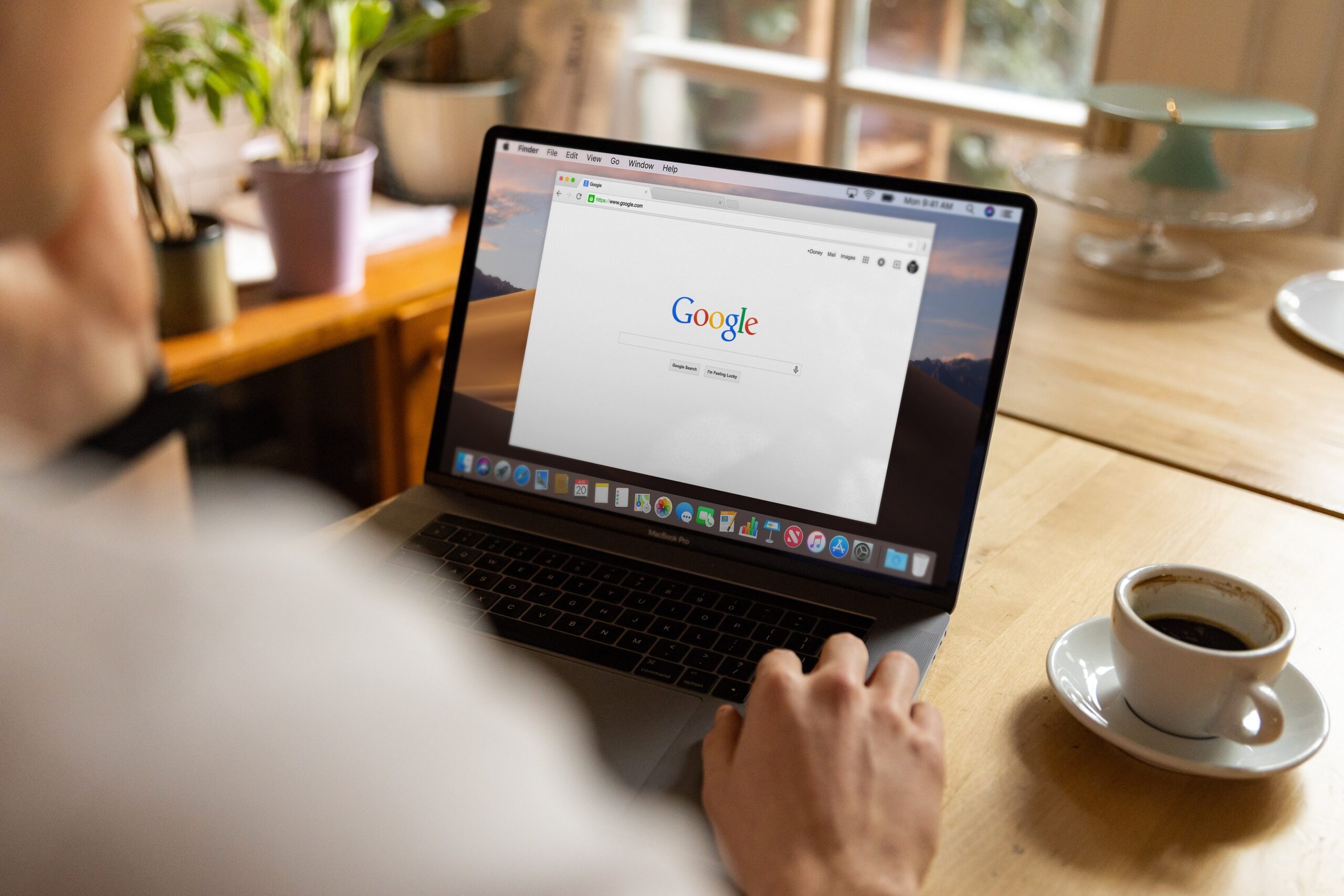 over shoulder of man using Google on laptop with a coffee.