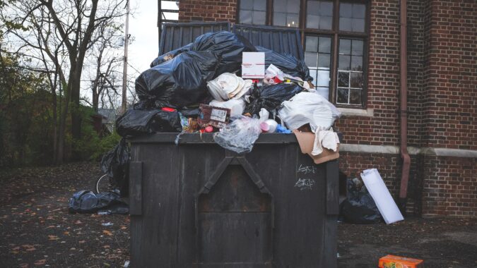 overflowing big four-wheel wheelie bin in front of building.