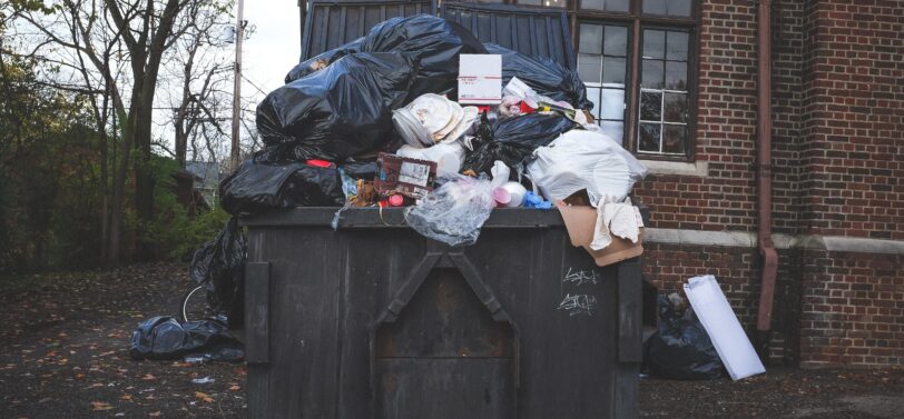 overflowing big four-wheel wheelie bin in front of building.