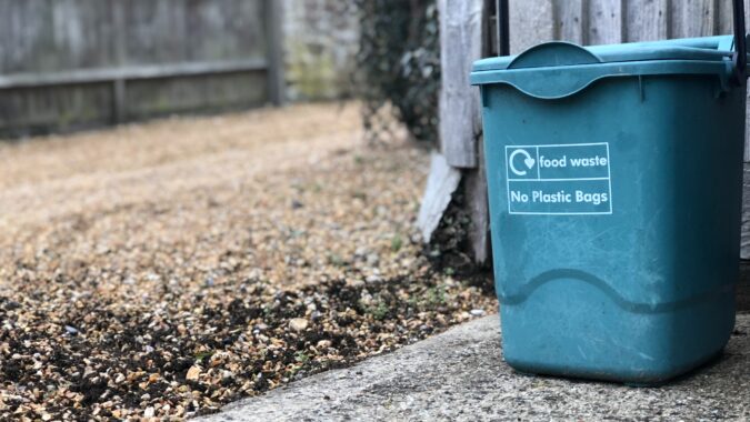 food waste bin next to a fence on driveway.