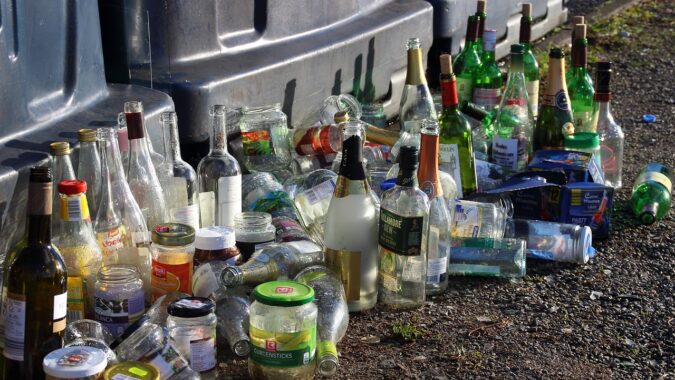 glass bottles and jars on the ground in front of recycling bins.