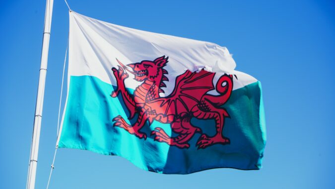 Welsh flag flying on a pole with blue sky background.