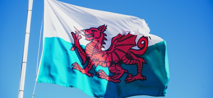 Welsh flag flying on a pole with blue sky background.